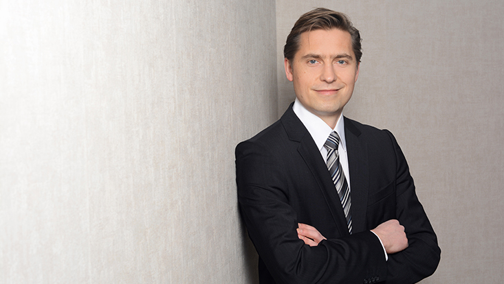 Herr Wenzlaff posiert mit verschränkten Armen vor einer Wand für ein Foto
