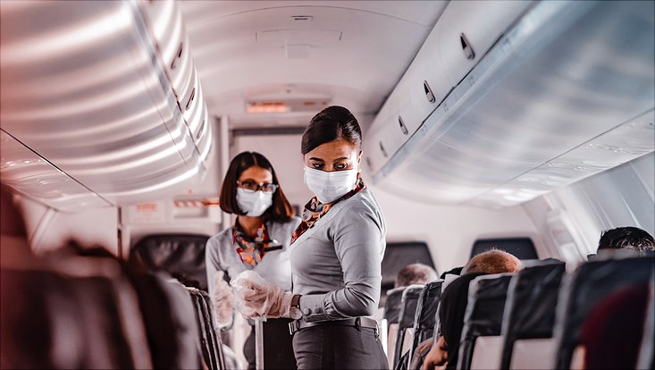 Two stewardesses with face mask handing out trinks from trolley in plane aisle