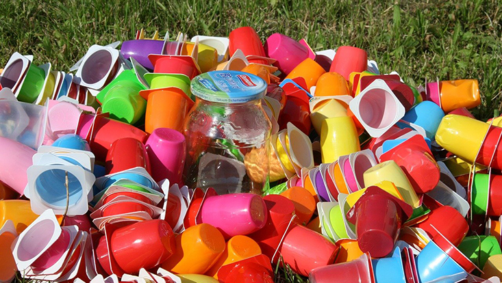 Viele bunte Joghurtbecher auf einer Wiese, dazwischen ein Pfand-Joghurtglas