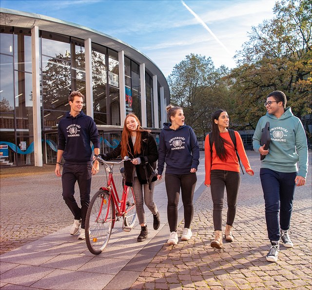 Zwei männliche und drei weibliche Studierende laufen am Campus in einer Reihe