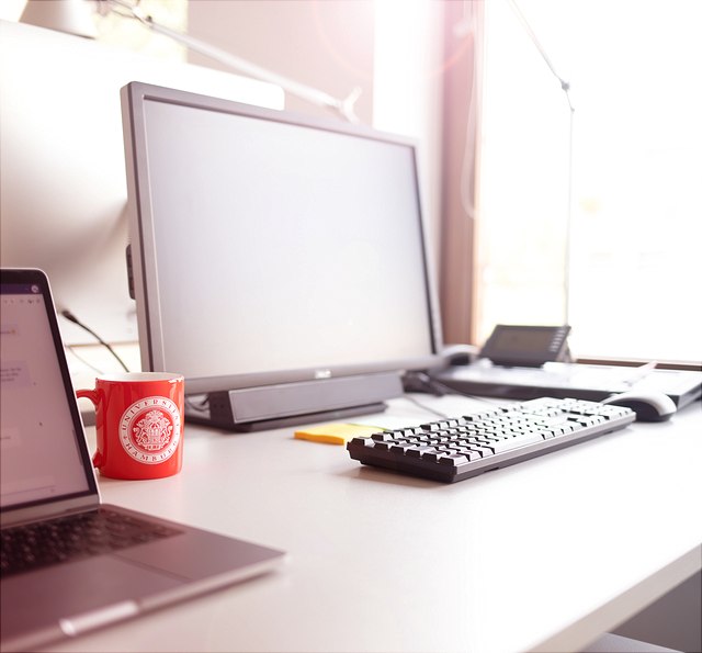 Arbeitsplatz mit PC und Laptop und roter Tasse