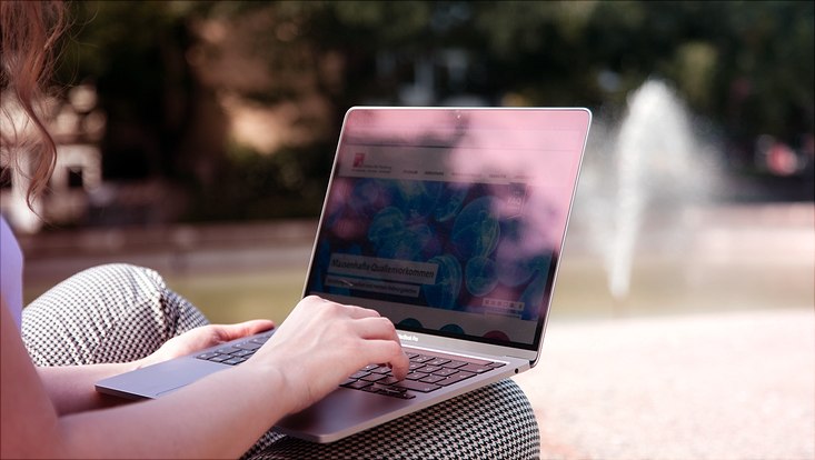 Studierende mit silbernem Laptop auf dem Schoß