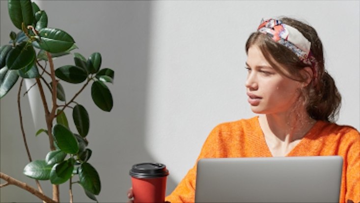 Junge Frau sitzt mit Kaffee vor einem Laptop.