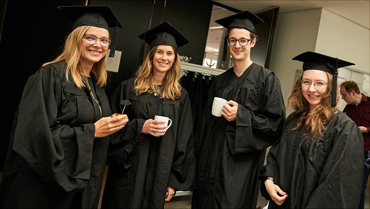 Dieses Bild zeigt drei Promovierte in ihren schwarzen Roben und Hüten