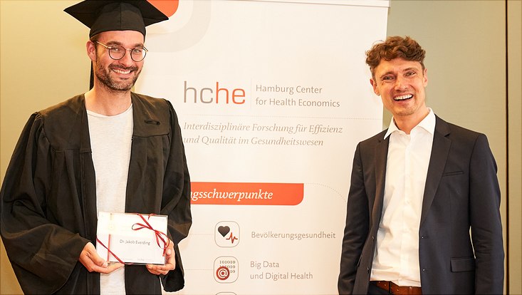 Auf diesem Bild sieht man Dr. Jakob Everding mit seinem Abschlussgeschenk und Prof. Dr. Jonas Schreyögg