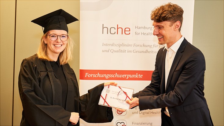 Auf diesem Bild sieht man Dr. Annika Schneider mit ihrem Abschlussgeschenk und Prof. Dr. Jonas Schreyögg
