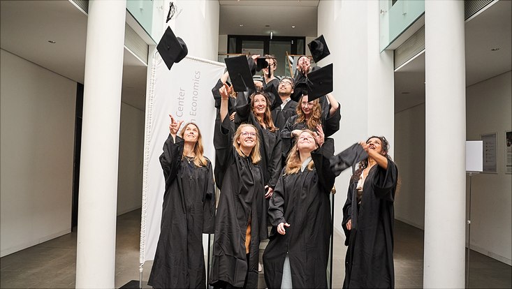 Auf diesem Bild sieht man die Promovierten in ihren schwarzen Roben, wie sie ihre Hüte in die Luft werfen