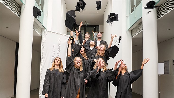 Auf diesem Bild sieht man die Promovierten in ihren schwarzen Roben, wie sie ihre Hüte in die Luft werfen