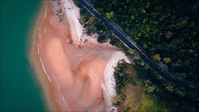 Foto auf dem links das Meer zu sehen ist, daneben ein Strand und rechts eine Straße