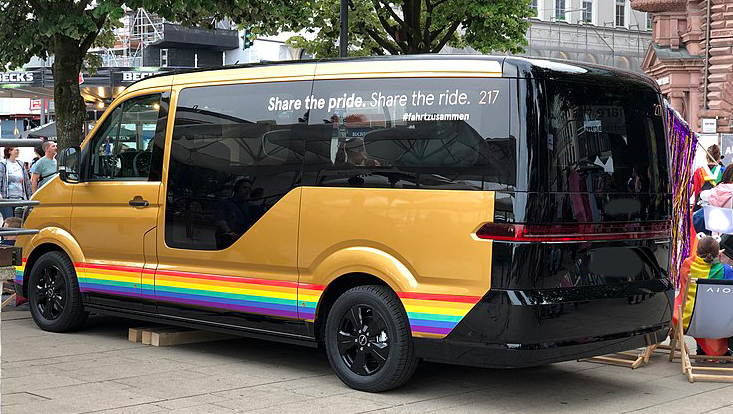 Kleinbus eines Ridepooling-Anbieters in den Farben gold und schwarz mit Regenbogenfarben verziert.