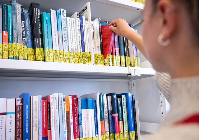 Eine Studentin greift nach Büchern in einem Regal der Bücherei.