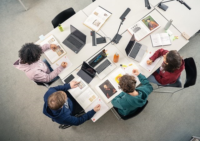 Eine Gruppe junger Menschen sitzt an mehreren Tischen und studiert Bücher, Vogelperspektive