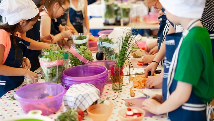 Kinder an einem Tisch. Kochkurs für Kinder. Kräuter und Gemüse.
