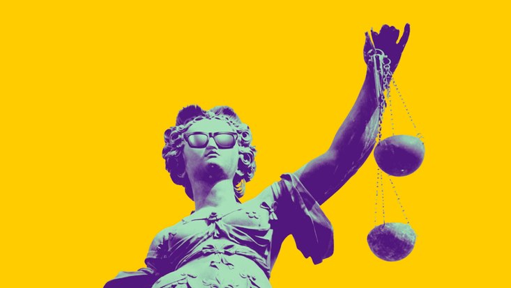 Justizia-Figur mit Augenbinde und Waage in der Hand vor gelbem Hintergrund