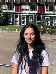 lächelnde junge Frau mit langen schwarzen Haaren vor einem gläsernen Gebäude