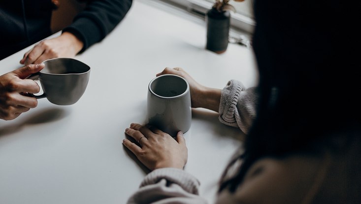Hände von zwei Personen, sitzend am Tisch mit Kaffeebechern