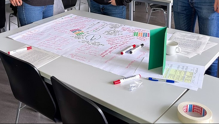 Menschen vor beschriebenem Flipchartpapier auf Tisch