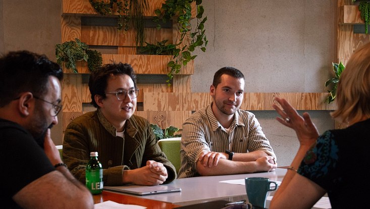 Mehrere Menschen sitzen gemeinsam an einem Tisch und hören einer Person zu