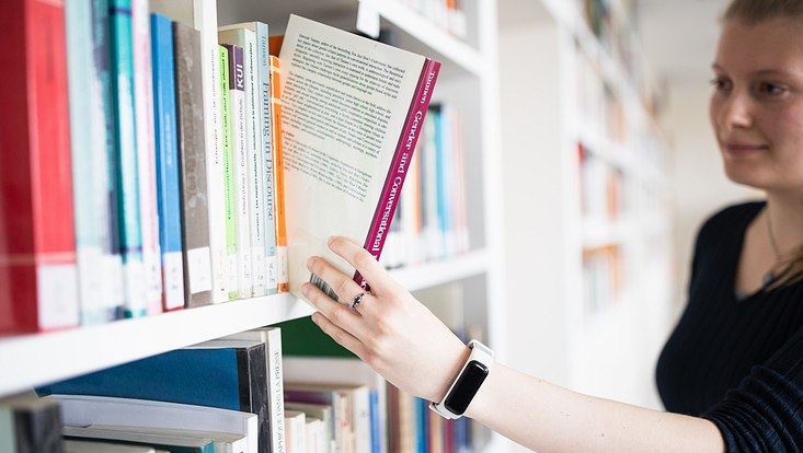 Studentin nimmt Buch aus dem Regal