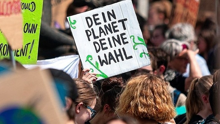 Köpfe von hinten auf Demo mit Schild "Dein Planet Deine Wahl"
