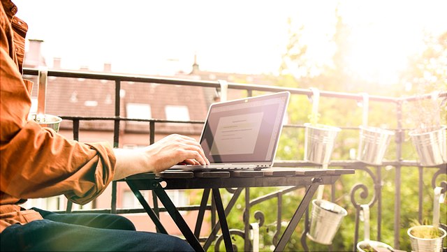 Person arbeitet auf dem Balkon am Laptop in der Sonne./Person working on a laptop on a balcony in the sun.