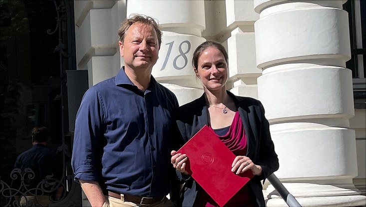 Frau Burmester und Prof. Clement vor dem Eingang des Haus der Betriebswirtschaft. Alexa Burmester hält Urkunde in der Hand
