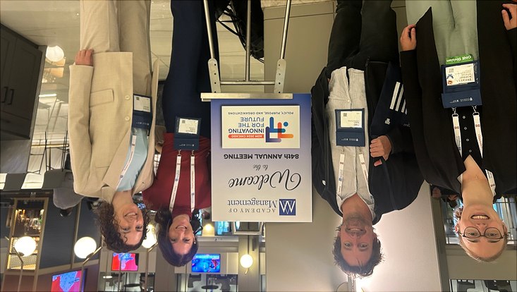 Das Bild zeigt vier Personen vor dem Banner der AOM Konferenz.