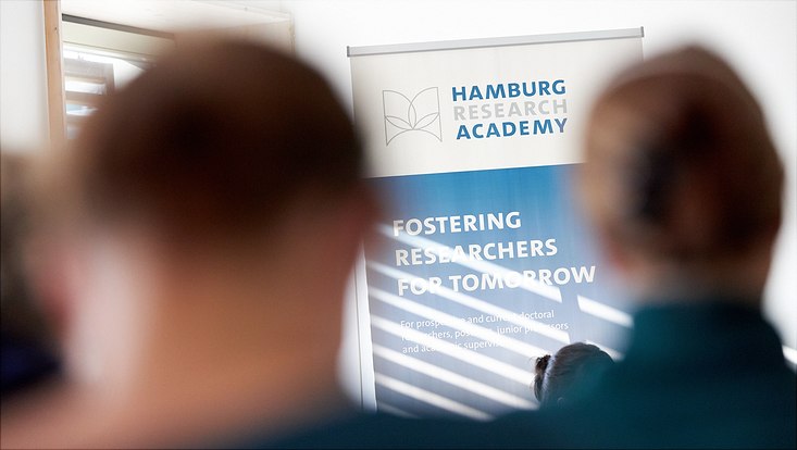 2 Personen blicken auf Roll up Banner der HRA