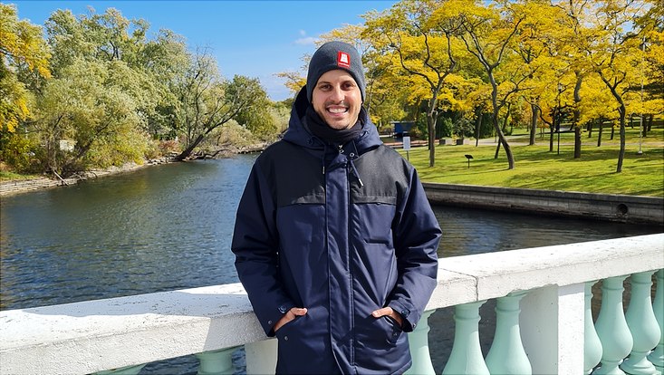 Foto von Hr. Gresse, der mit Winterjacke und Mütze auf einer Brücke im Park steht, im Hintergrund sichtbar der Park mit Fluss