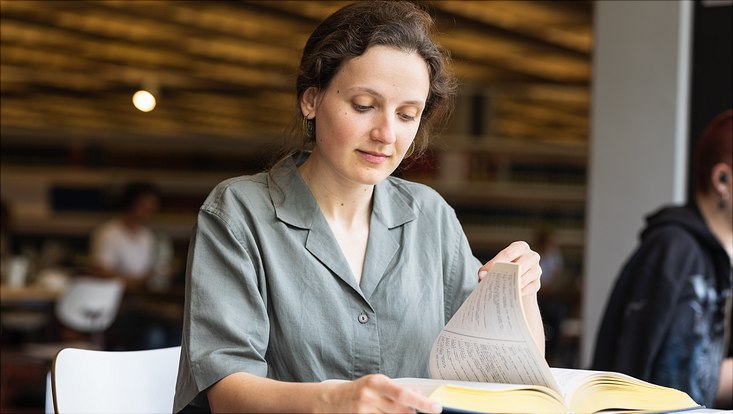 Studentin in der Bibliothek mit Buch