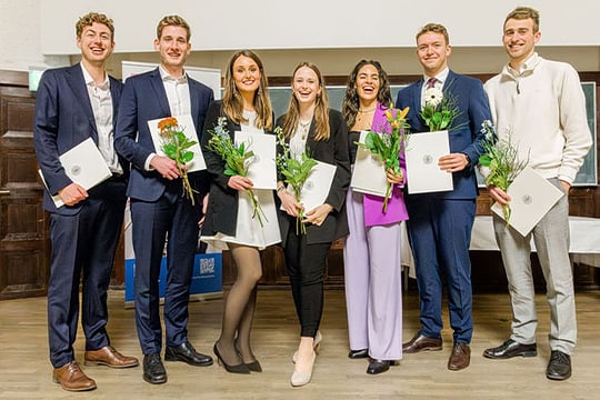 Studiernende mit ihrem Abschlussurkunden auf einer Bühne