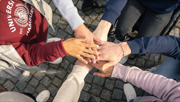 Diverse Menschen, die ihre Hände in die Mitte halten.