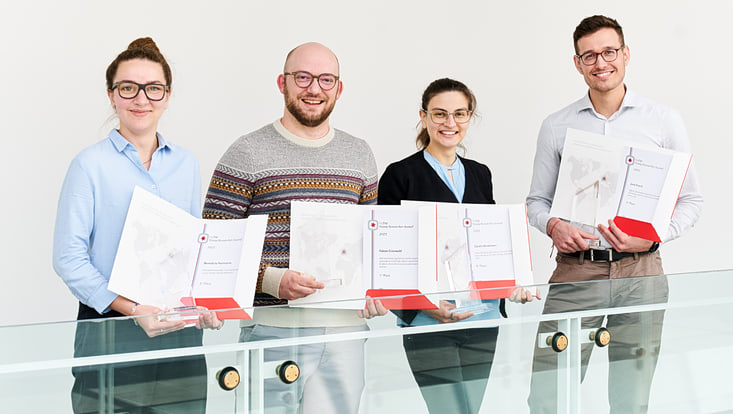 Four doctoral students holding awards and certificates.