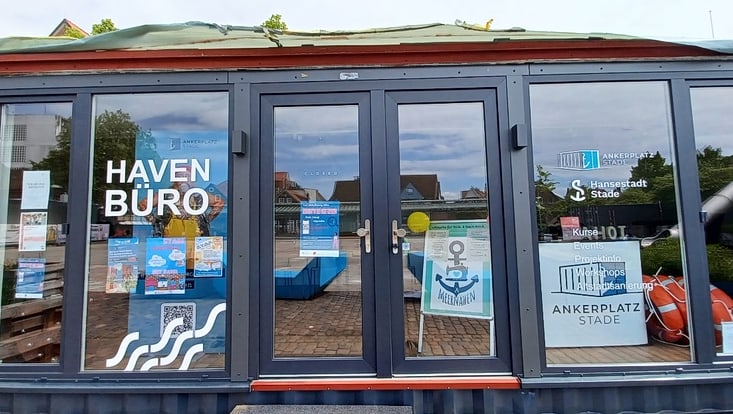 Das Havenbüro des Ankerplatz Stade e. V., Anlaufstelle, Büro und Multifunktionsraum. Als Dorfbewohner:in per App zugänglich. Gespiegelt sind Sitzgelegenheiten, Pflanzkisten und die Rutsche der „Butcherbox“ zu sehen.