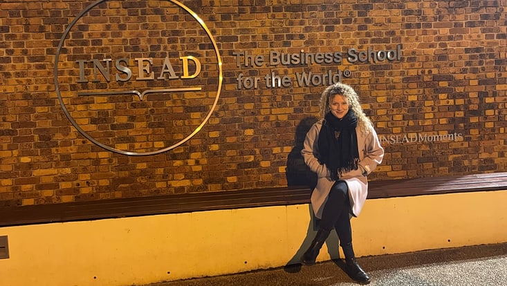 Julia Diana Lenk sitzt auf Bank vor INSEAD Logo
