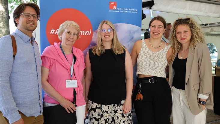 Frauen und ein Mann vor einem Uni Alumni Roll-up