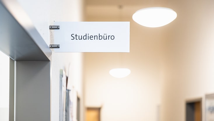 Weißes Schild auf dem in schwarzer Schrift Studienbüro steht.