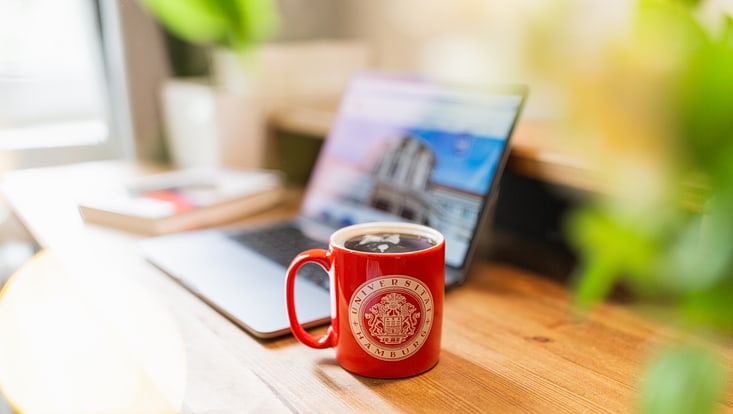 Rote UHH-Tasse vor einem Laptop auf einem Schreibtisch