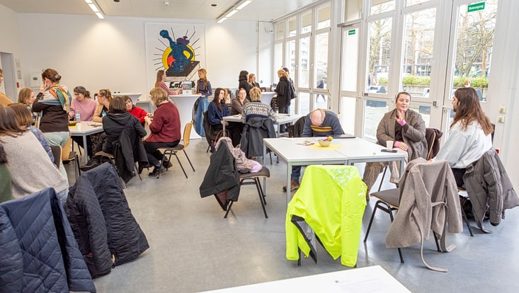 Verschiedene Personen an Tischen in Seminarraum