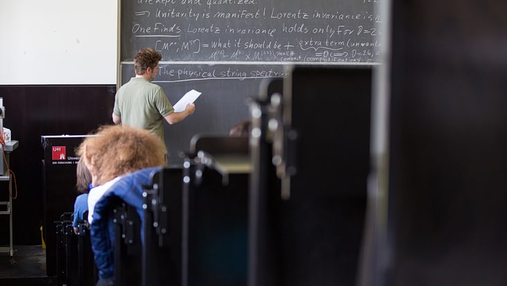 männliche Person vor Tafel in Hörsaal