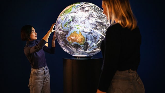 Symbolbild Globus mit 2 Wissenschaftlerinnen