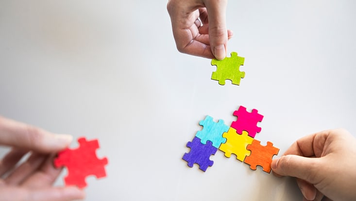 drei Hände legen unterschiedlich farbene Puzzeteile zusammen