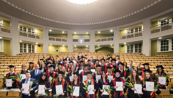 buisness-school-rajele.photography-2-733x414 Viele junge Menschen stehen in einem Hörsaal und halten ihre Abschlusszeugnisse in die Kamera