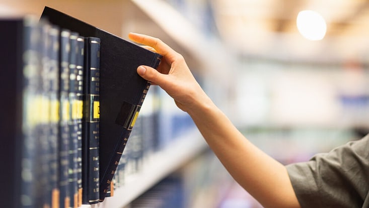 Eine Hand nimmt ein Buch aus dem Bücherregal.
