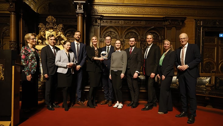 Männer und Frauen im Rathaus vor dunkelrotem und goldenen Hintergrund