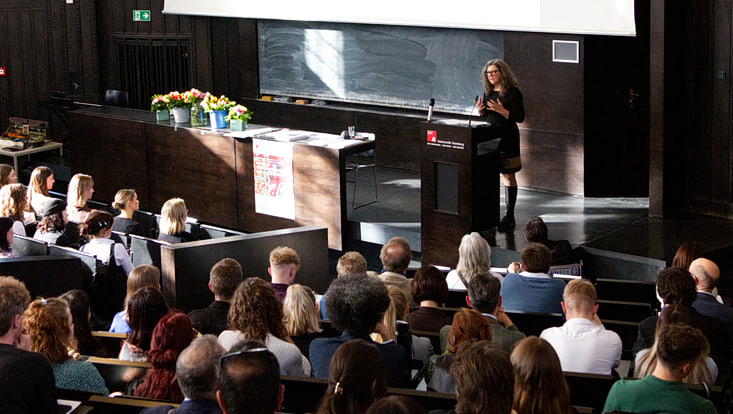Symbolbild Absolvent:innenfeier: Blick von hinten in einen Hörsaal, unten am Pult spricht Prof. Anita Engels