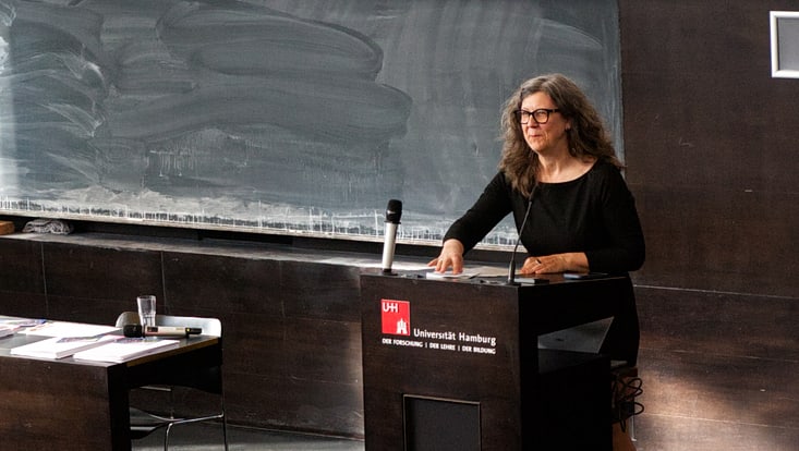 Symbolbild Absolvent:innenfeier: Blick von hinten in einen Hörsaal, unten am Pult spricht Prof. Anita Engels