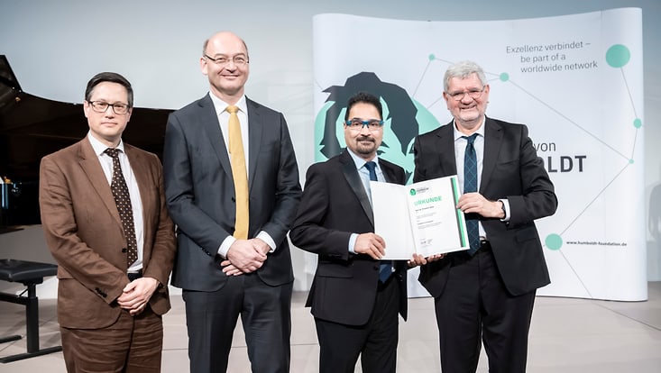Männer bei Preisverleihung vor Aufsteller