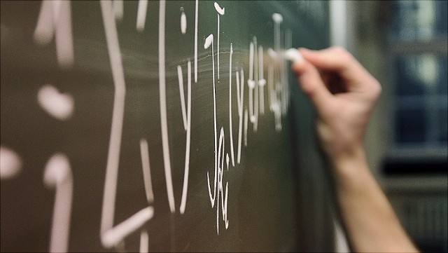 Detail einer Hand, die mit Kreide eine mathematische Formel an eine Tafel schreibt
