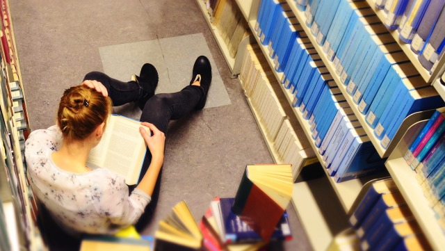 Frau liest Bücher auf dem Boden zwischen Bücherregalen/Women reading on the floor between bookshelfs